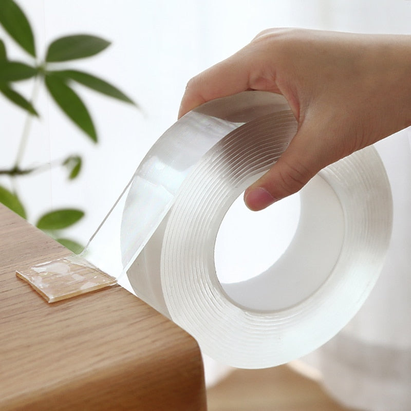 A roll of clear double-sided nano tape being applied to a surface, with a hand holding the tape. The tape appears transparent and smooth.