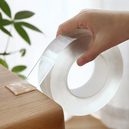 A roll of clear double-sided nano tape being applied to a surface, with a hand holding the tape. The tape appears transparent and smooth.